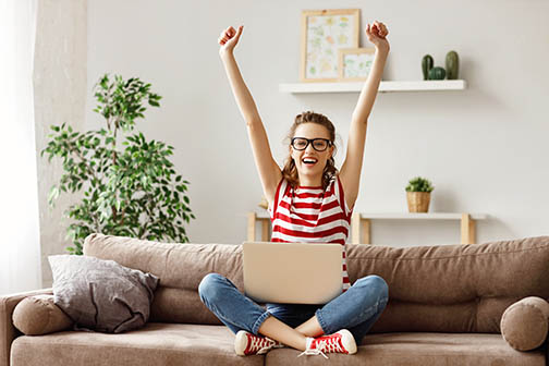 Glad student celebrating good news while working on laptop at home
